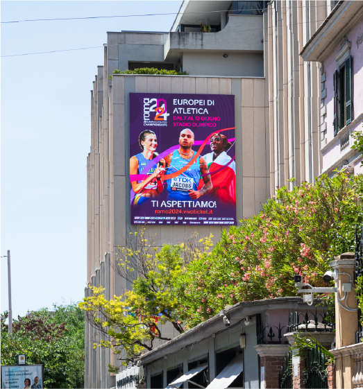 Cartellone degli Europei di atletica Roma 2024 affisso su un edificio cittadino, con atleti in primo piano e colori vivaci.