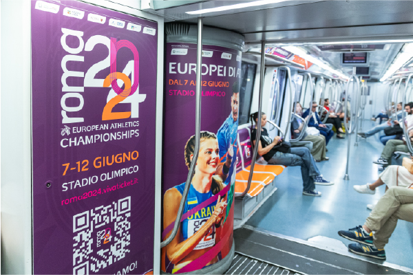 Pubblicità degli Europei di atletica Roma 2024 all’interno di una carrozza della metropolitana, con passeggeri seduti.