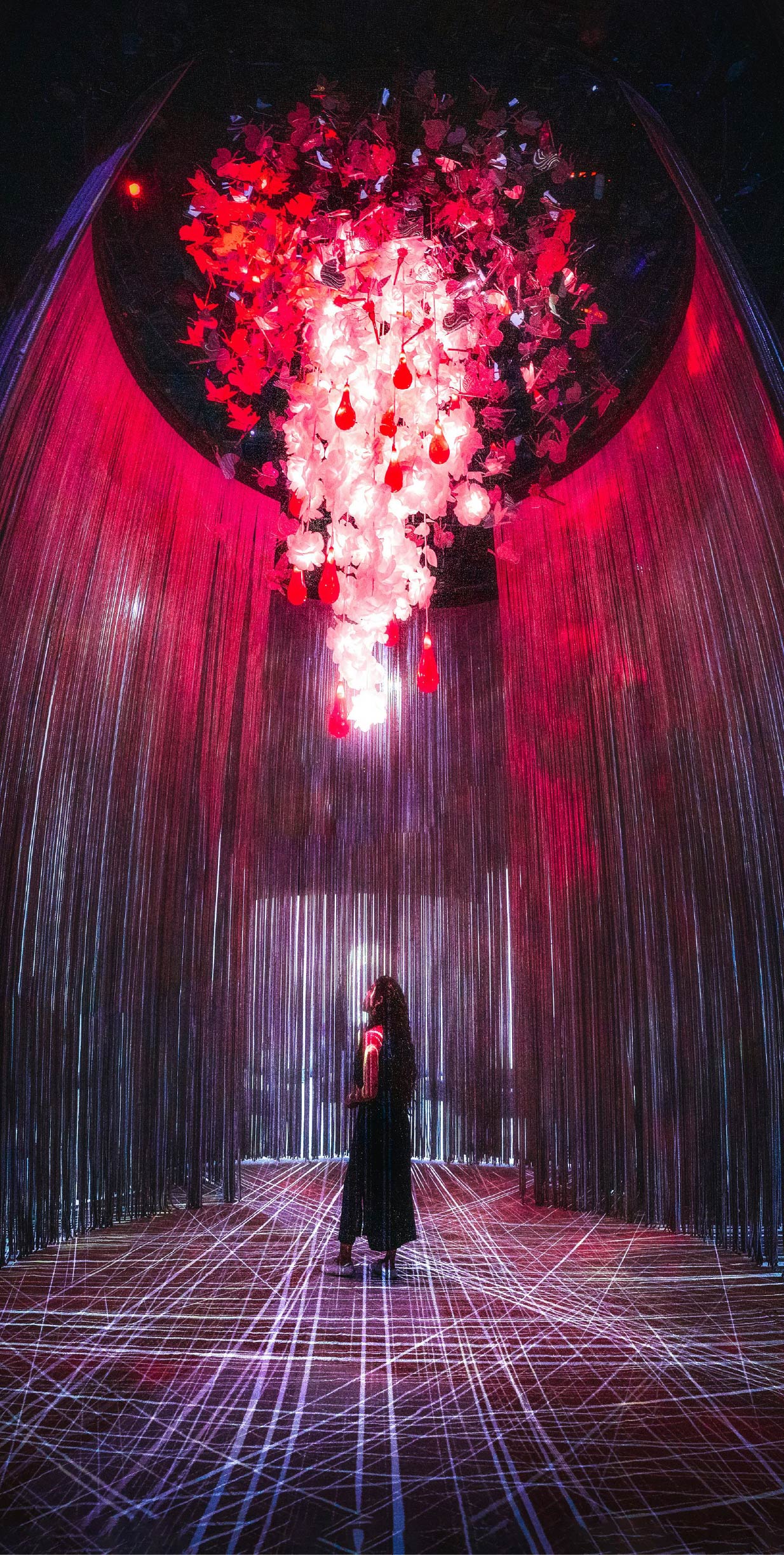 Installazione artistica immersiva con scultura sospesa rossa e bianca e proiezioni luminose nel pavimento, vista in una mostra
