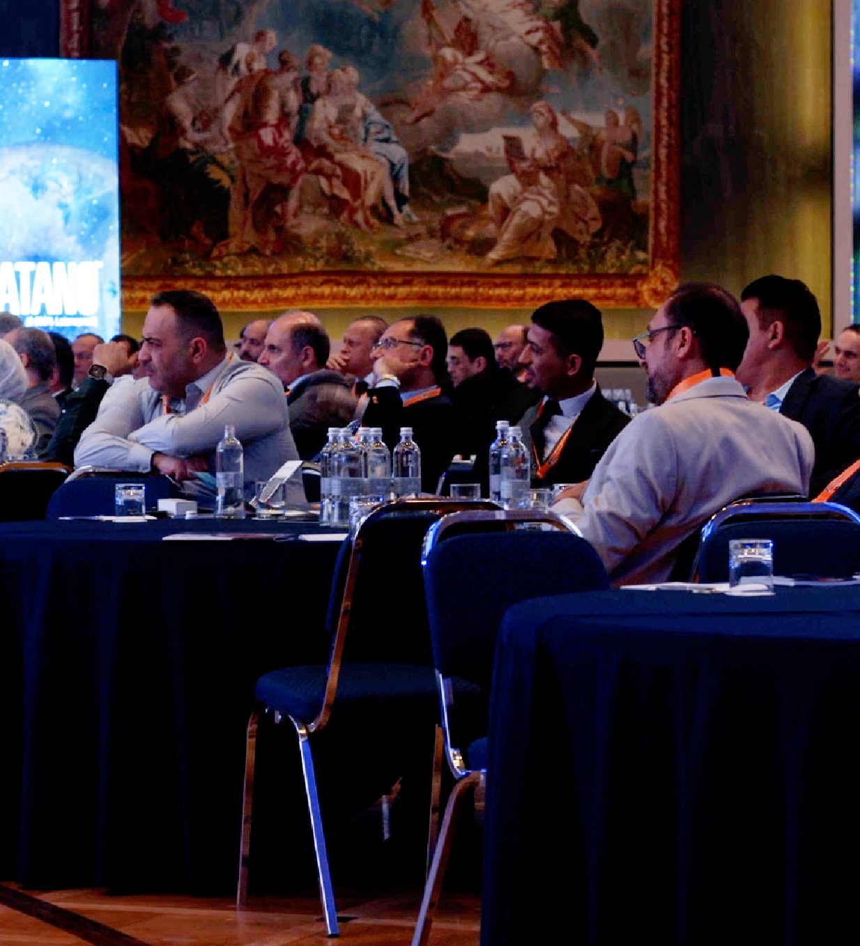 Persone in un meeting aziendale sedute ai tavoli di una sala conferenze con schermo e presentazione sullo sfondo